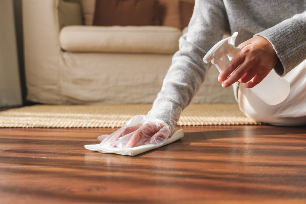 Closeup image of a woman wearing protective glove, cleaning and washing wooden floor at home