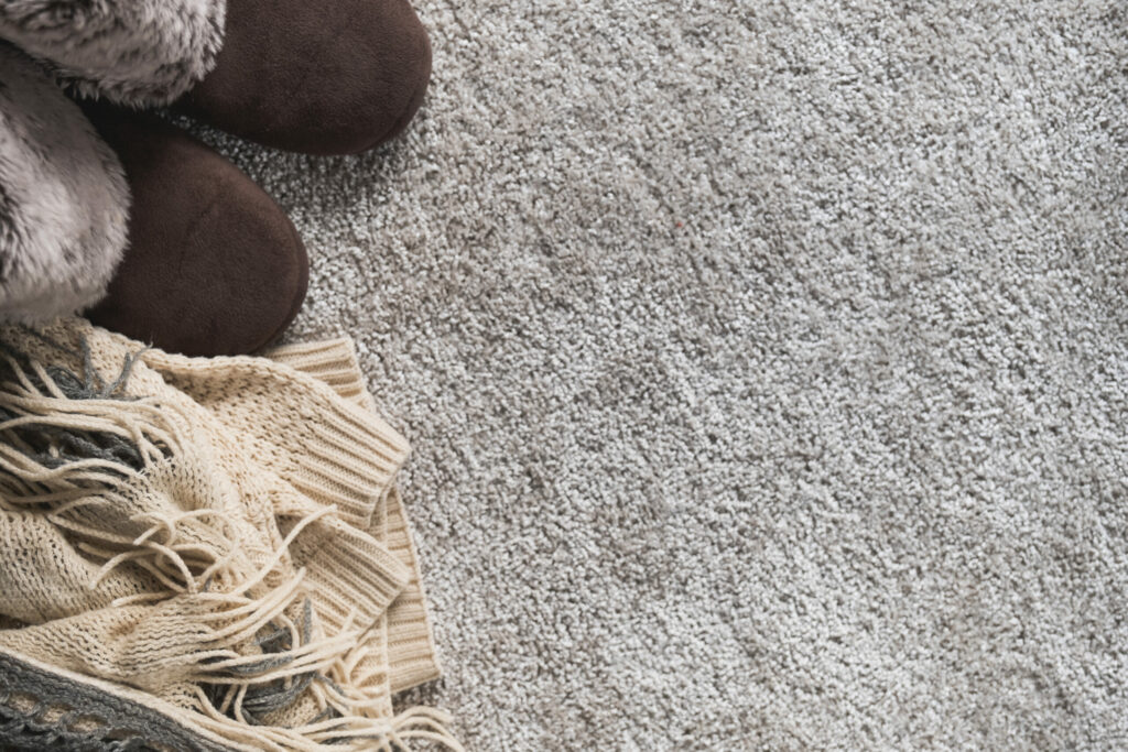 Cozy winter background with warm clothes in beige color. Sweater, scarf and slippers in scandinavian style.