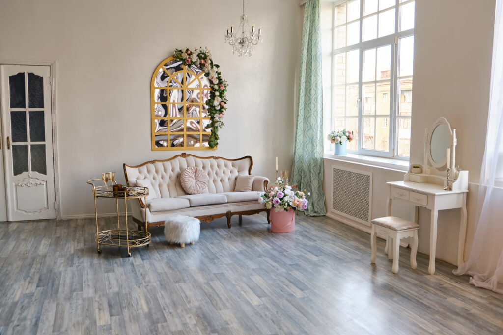Luxurious beautiful classical white interior, a sofa with pillows, a mirror, a table on wheels, a vintage chandelier, a fluffy pouffe, boudoir table, all decorated with decorative flowers. Retro, classics