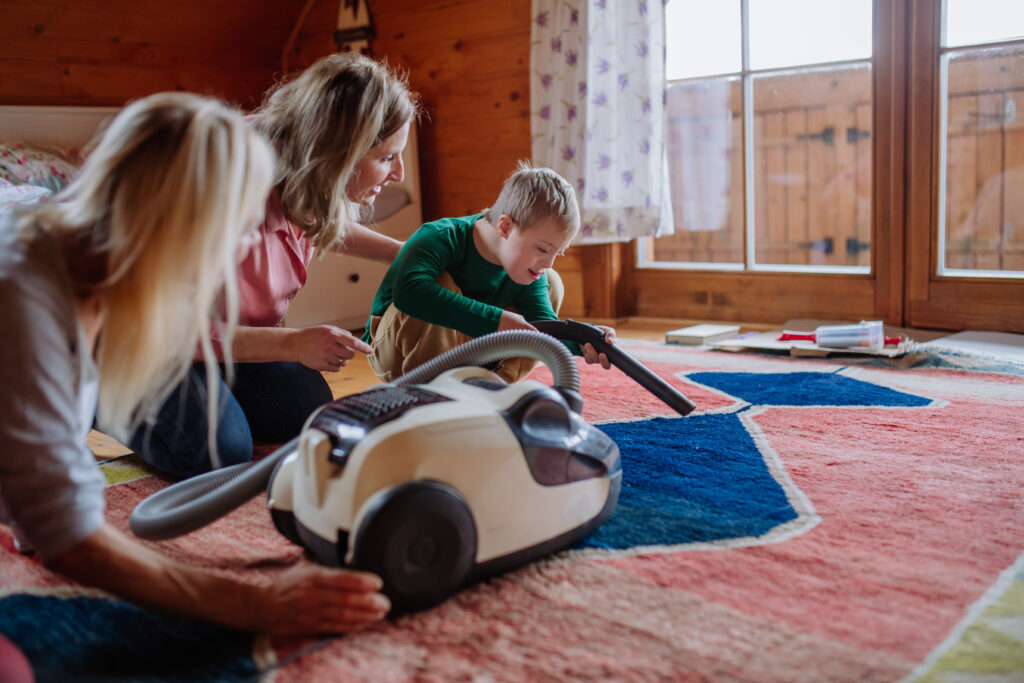 Boy with Down syndrome with his mother and grandmother vacuum cleaning at home