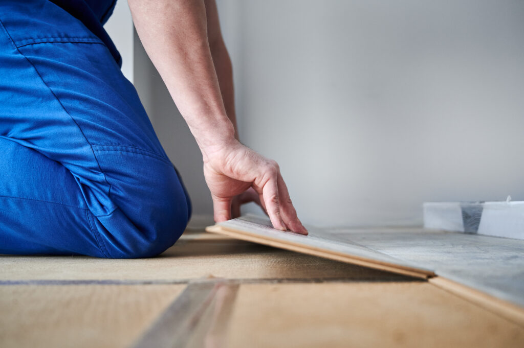 Male hands laying laminate wood plank on floor underlayment. Close up of man construction worker installing laminate timber flooring in apartment under renovation. Hardwood floor renovation concept.