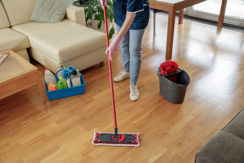 Unrecognizable woman washing floor with mop in living room. Professional house cleanup concept