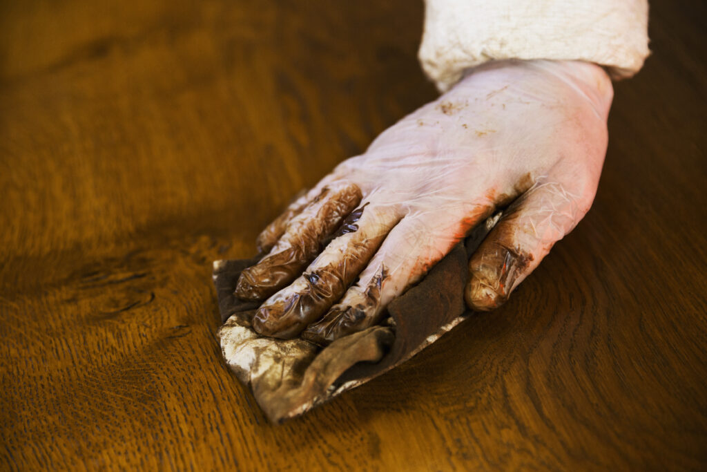 England,Close up of a carpenter wearing protective gloves, applying varnish onto a wooden surface with a cloth.